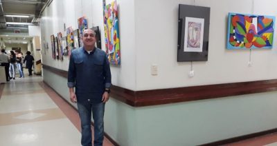 Artista posa em frente ao corredor com suas telas